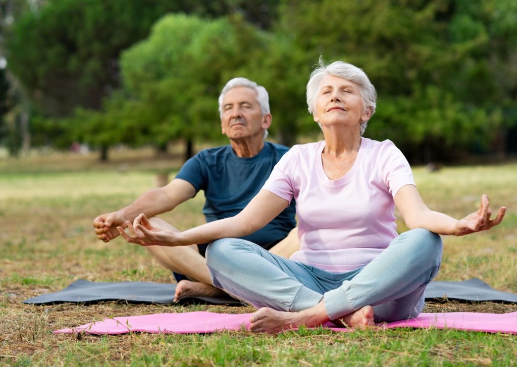 Starsza kobieta i mężczyzna wykonują ćwiczenia oddechowe na świeżym powietrzu.